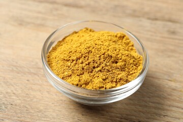 Curry powder in bowl on wooden table, closeup