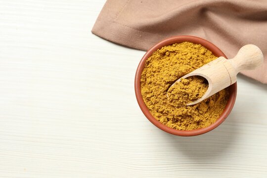 Curry powder in bowl and scoop on white wooden table, top view. Space for text