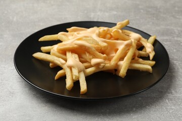 Delicious French fries with cheese sauce on grey table, closeup