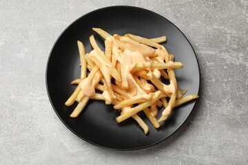 Delicious French fries with cheese sauce on grey table, top view