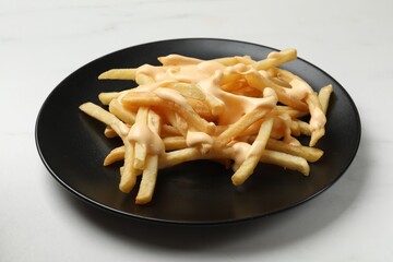 Delicious French fries with cheese sauce on white table, closeup