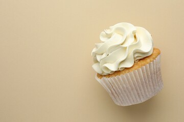 Tasty vanilla cupcake with cream on beige background, top view. Space for text