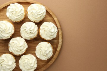 Tasty vanilla cupcakes with cream on dark beige background, top view. Space for text