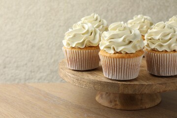 Tasty vanilla cupcakes with cream on wooden table, space for text