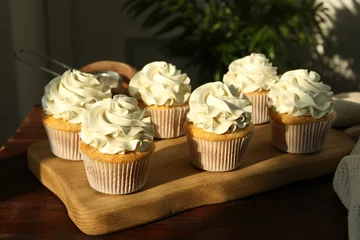 Poster Tasty cupcakes with vanilla cream on wooden table, closeup © New Africa