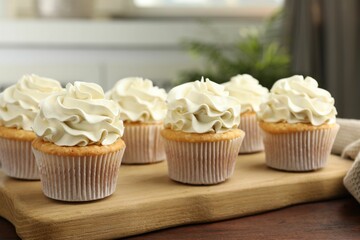 Tasty cupcakes with vanilla cream on wooden table, closeup