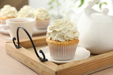 Tasty cupcake with vanilla cream and teapot on light wooden table, closeup
