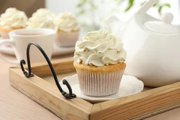 Rolgordijnen Tasty cupcake with vanilla cream and teapot on light wooden table, closeup © New Africa