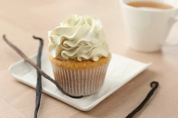 Rolgordijnen Tasty cupcake with cream and vanilla pods on light wooden table, closeup © New Africa