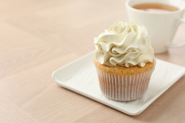 Tasty cupcake with vanilla cream on light wooden table, closeup. Space for text