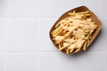 Poster Delicious French fries with cheese sauce on white tiled table, top view. Space for text © New Africa