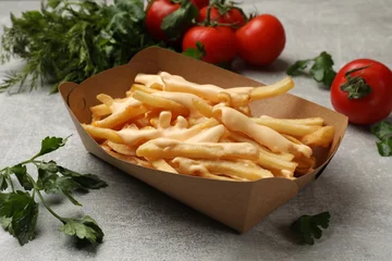 Rolgordijnen Tasty potato fries, cheese sauce in paper container and products on grey table, closeup © New Africa