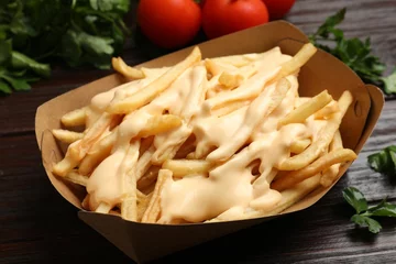Raamstickers Tasty potato fries, cheese sauce in paper container and products on wooden table, closeup © New Africa