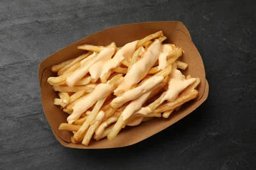 Rolgordijnen Tasty potato fries and cheese sauce in paper container on black table, top view © New Africa