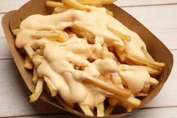 Keuken spatwand met foto Tasty potato fries and cheese sauce in paper container on light wooden table, closeup © New Africa