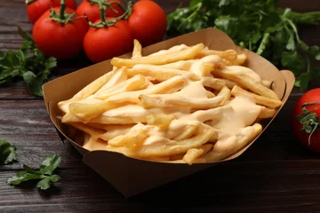 Poster Tasty potato fries, cheese sauce in paper container and products on wooden table, closeup © New Africa