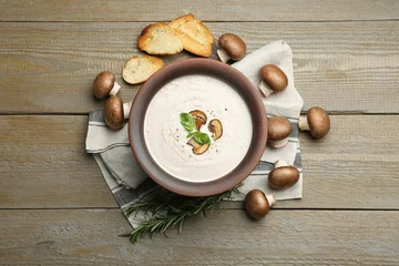 Tuinposter Tasty homemade mushroom soup in ceramic pot, croutons, fresh champignons and rosemary on wooden table, flat lay © New Africa