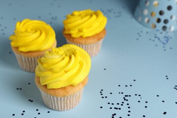 Delicious cupcakes with bright cream and confetti on light blue background, closeup. Space for text