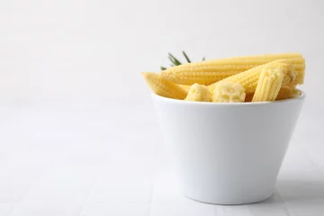 Poster Tasty fresh yellow baby corns in bowl on white tiled table, space for text © New Africa