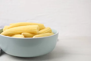 Gordijnen Tasty fresh yellow baby corns in bowl on white wooden table, closeup. Space for text © New Africa