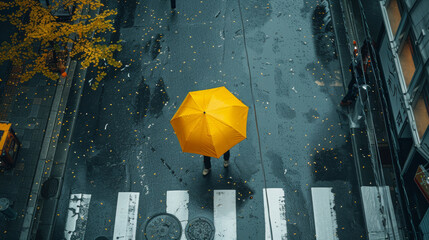 A person is walking down a street with a yellow umbrella. The street is wet and there are leaves on the ground