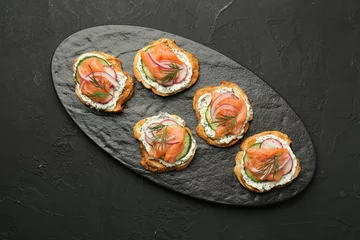 Poster Tasty canapes with salmon, cucumber, radish and cream cheese on black table, top view © New Africa