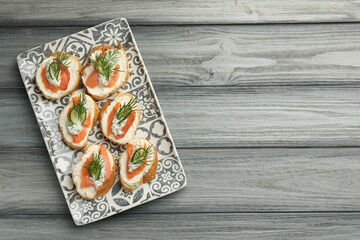 Tasty canapes with salmon, cucumber, cream cheese and dill on wooden table, top view. Space for text