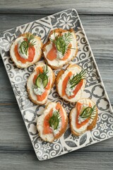 Tasty canapes with salmon, cucumber, cream cheese and dill on wooden table, top view