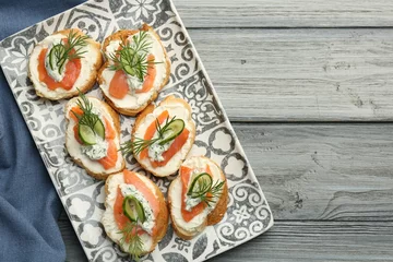 Poster Tasty canapes with salmon, cucumber, cream cheese and dill on wooden table, top view. Space for text © New Africa