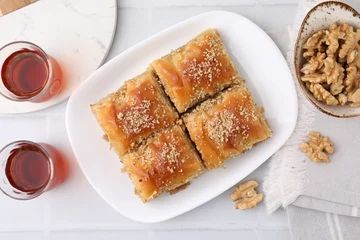  Eastern sweets. Pieces of tasty baklava, walnuts and tea on white tiled table, flat lay © New Africa