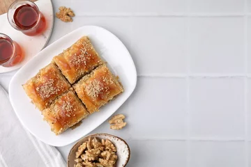 Zelfklevend Fotobehang Eastern sweets. Pieces of tasty baklava, walnuts and tea on white tiled table, flat lay. Space for text © New Africa