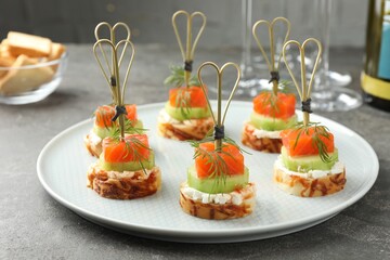 Tasty canapes with salmon, cucumber, bread and cream cheese on grey table