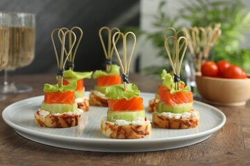Tasty canapes with salmon, cucumber, bread and cream cheese on wooden table, closeup
