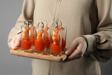 Deurstickers Woman holding tasty canapes with shrimps, tomatoes and sauce in shot glasses on grey background, closeup © New Africa