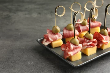 Plexiglas foto achterwand Tasty canapes with olives, prosciutto and cheese on grey table, closeup. Space for text © New Africa