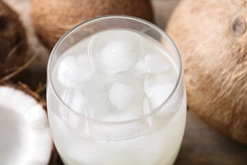 Glass of coconut water, ice cubes and nuts on wooden table, closeup