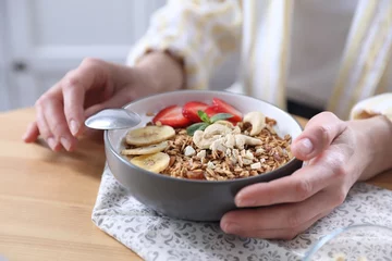 Outdoor kussens Woman eating tasty granola with banana, cashew and strawberries at wooden table indoors, closeup © New Africa