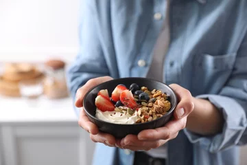 Gordijnen Woman holding bowl of tasty granola with berries, yogurt and seeds indoors, closeup © New Africa