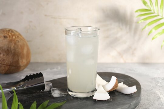 Glass of coconut water, ice cubes and nuts on grey table