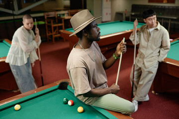 Portrait of African American adult man wearing hat with multiethnic group of people in pool club - 783117648