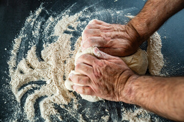 Männerhände kneten massieren und rollen einen Teig auf einer Arbeitsoberfläche in der Küche zu Hause aus