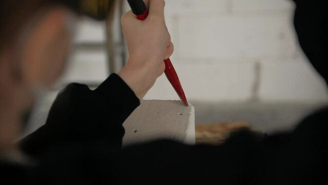 Close-up of man's hands creating a stone sculpture using a chisel and hammer in a workshop.