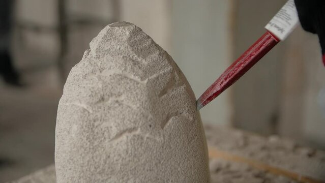 Close-up of man's hands creating a stone sculpture using a chisel in a workshop.