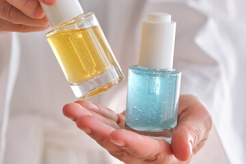 Two yellow and blue serums in a womans hands in a robe.