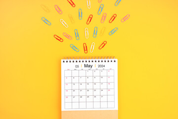 May 2024 desk calendar and colorful metal paperclips on yellow background. - obrazy, fototapety, plakaty