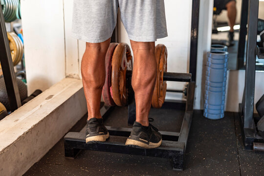Dedicated anonymous man at the gym setting does calf raises on a weight-loaded machine with plates, focusing on lower body strength.