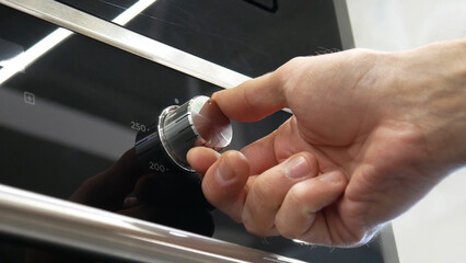 Close-up of a male hand turning on an electronic oven