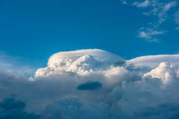 Huge dramatic lenticular cloud on white lush cloudy hill in blue sky. Beautiful cloudscape with big UFO shaped cloud in center. Scenic skyscape with altocumulus clouds. Awesome unusual cloudy skies. - 783127014