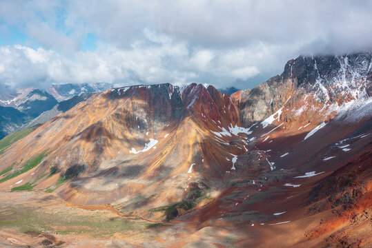 Scenic aerial view to rounded multicolor valley with curved iron river and big sharp rocky ridge of red color. Colorful large mountain range in freshly fallen snow. Vivid scenery with high mountains.