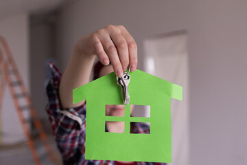Woman holding paper house symbol and keys in front of camera, new home concept, background blurred. High quality photo